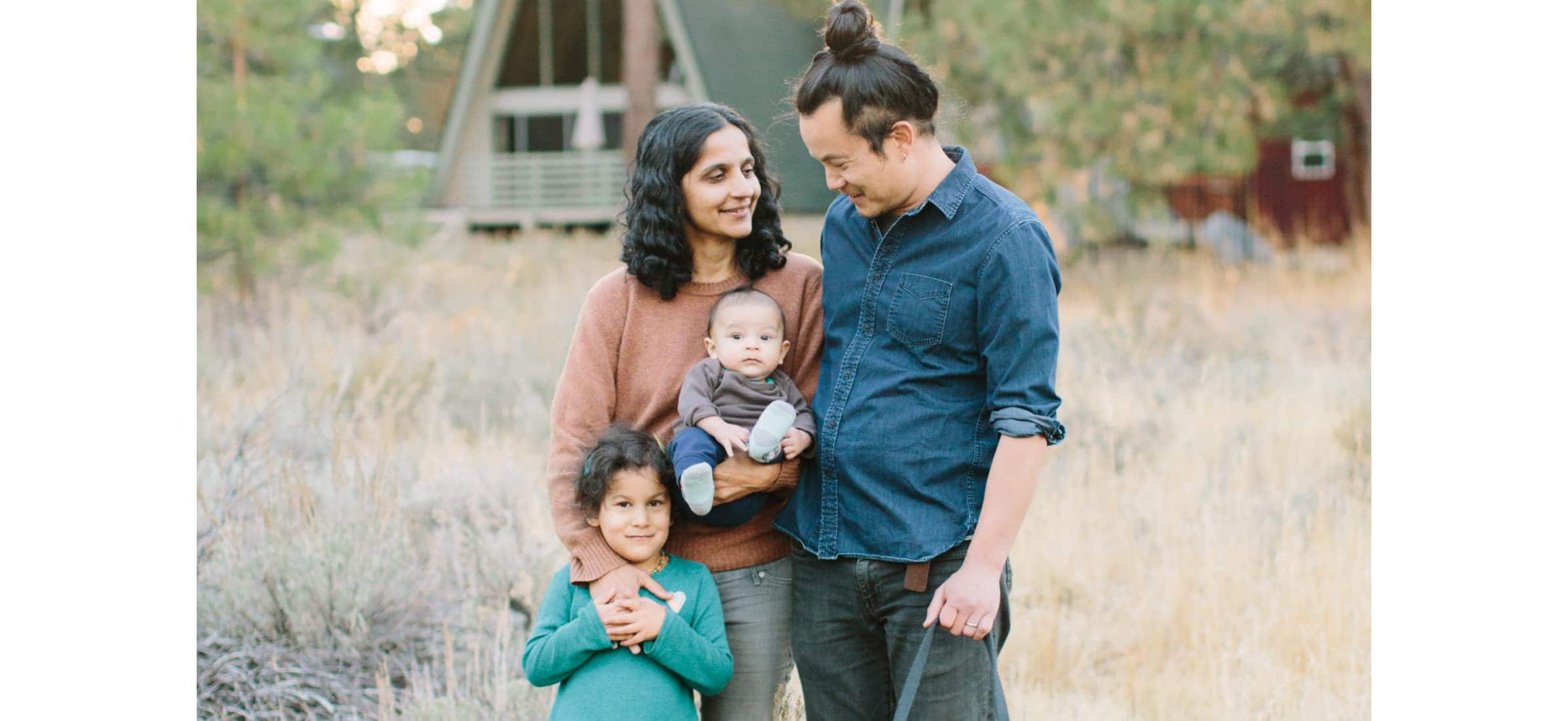 Burton Li stands in a field in front of his home, with his wife, baby and young daughter.